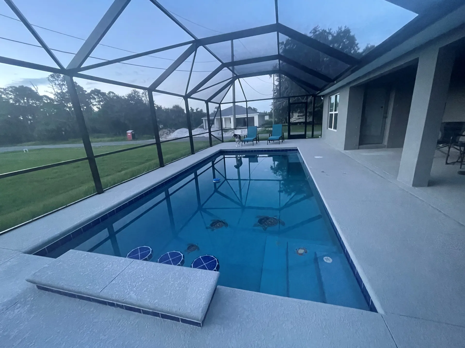 Screen enclosure over a rural pool with a raised bench wall and covered lanai