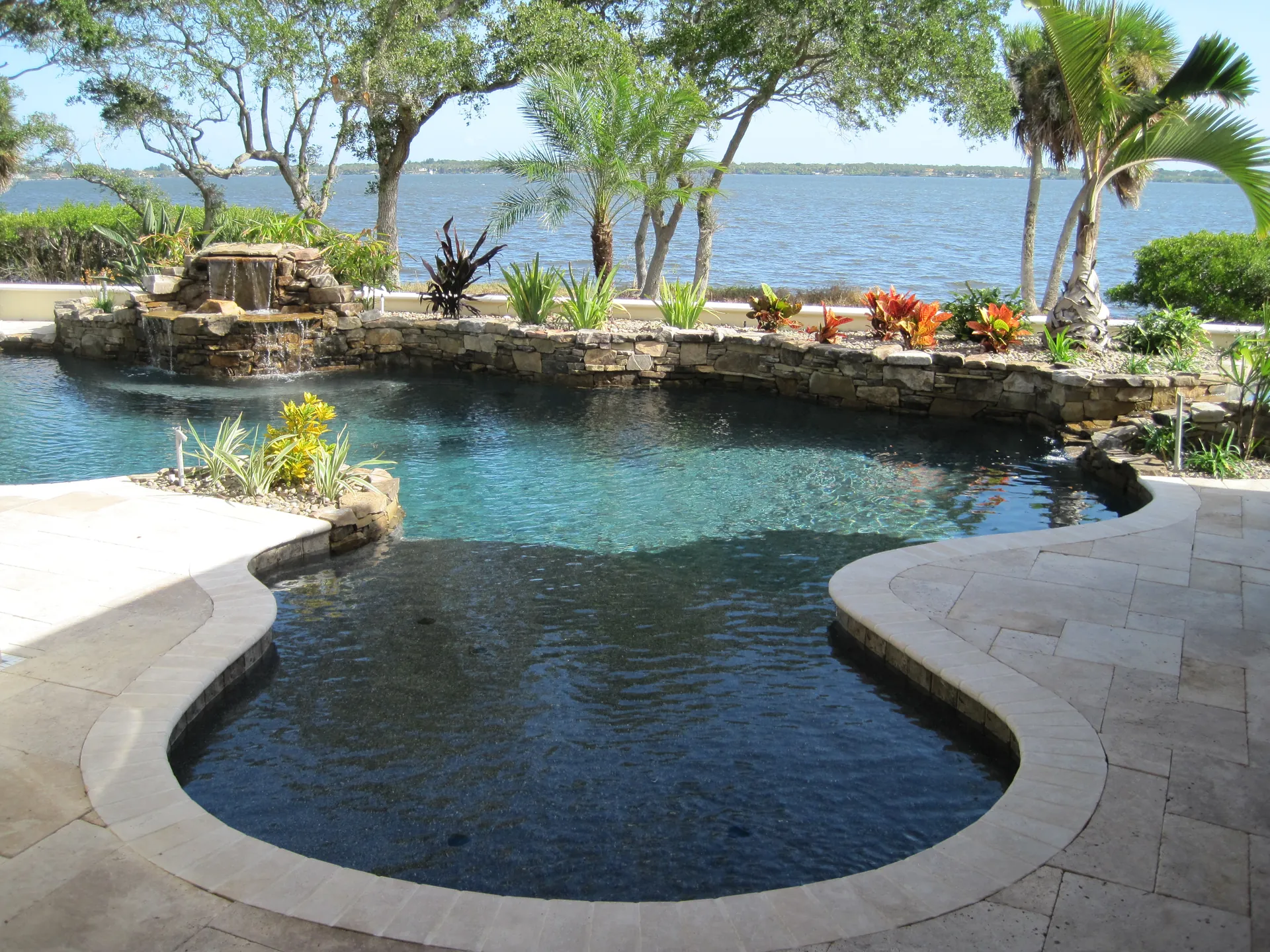 Freeform dark bottom pool with a rock waterfall overlooking the river