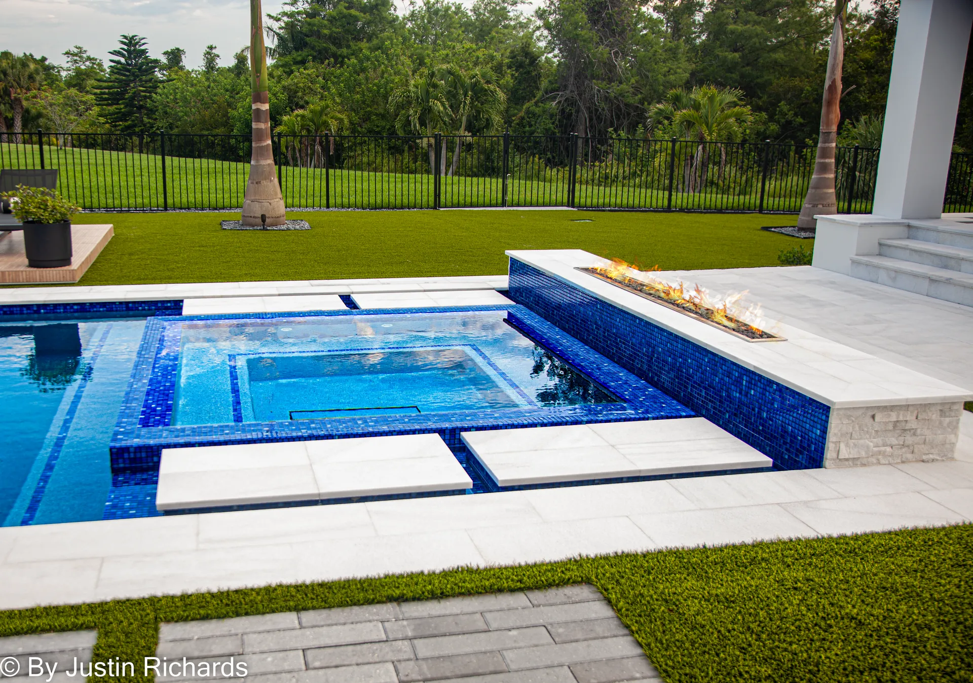 Royal blue glass tile spa with a lit linear fire feature after a remodel